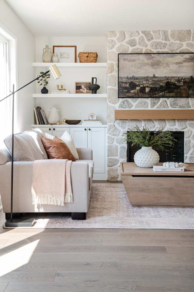 designer living room with stone fireplace, storage ottoman and built in floating shelves